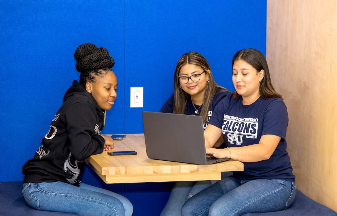 Three students in the student center looking at a laptop.